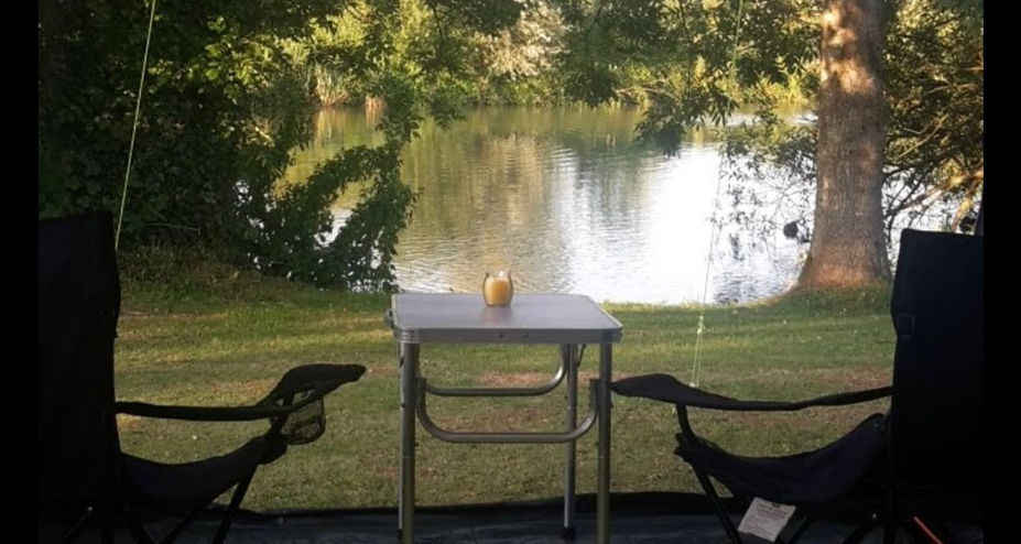 Two camping chairs and a table looking out over the lake, shaded by trees